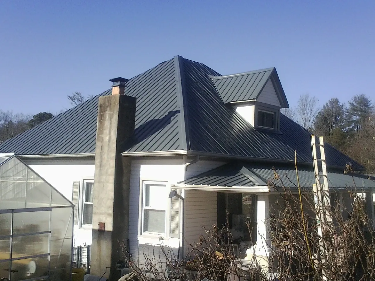 Dark blue standing seam metal roof on a white farmhouse with dormer — Slate & Tile Roof Repair by Roofing Brothers in Rollinsville
