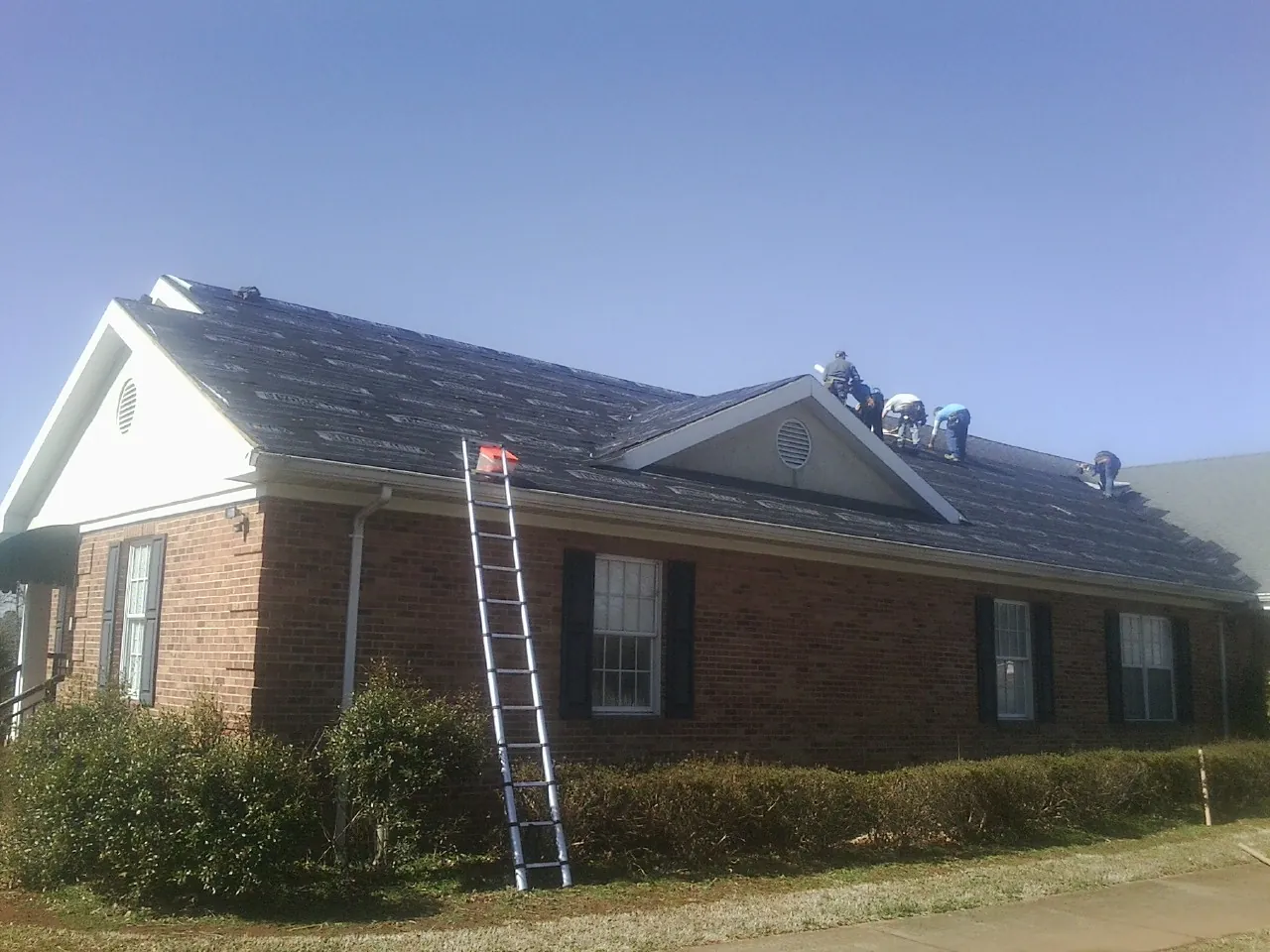 Crew tearing shingles off a brick ranch roof with a ladder set — Metal Roof Repair work by our crew in Rollinsville