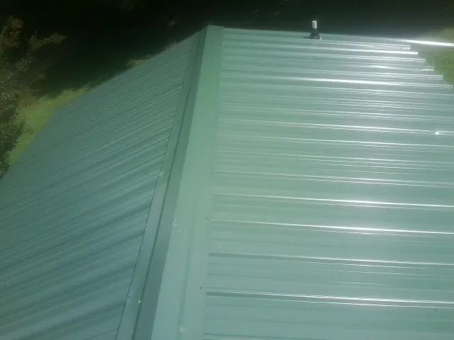 New green metal panels meeting at the ridge of a roof — Flat Roof Repair work by our crew in Rollinsville