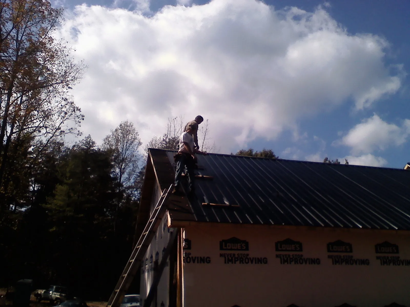 Roofer fastening dark metal panels high against a cloudy sky, from a Roof Inspection job in Rollinsville