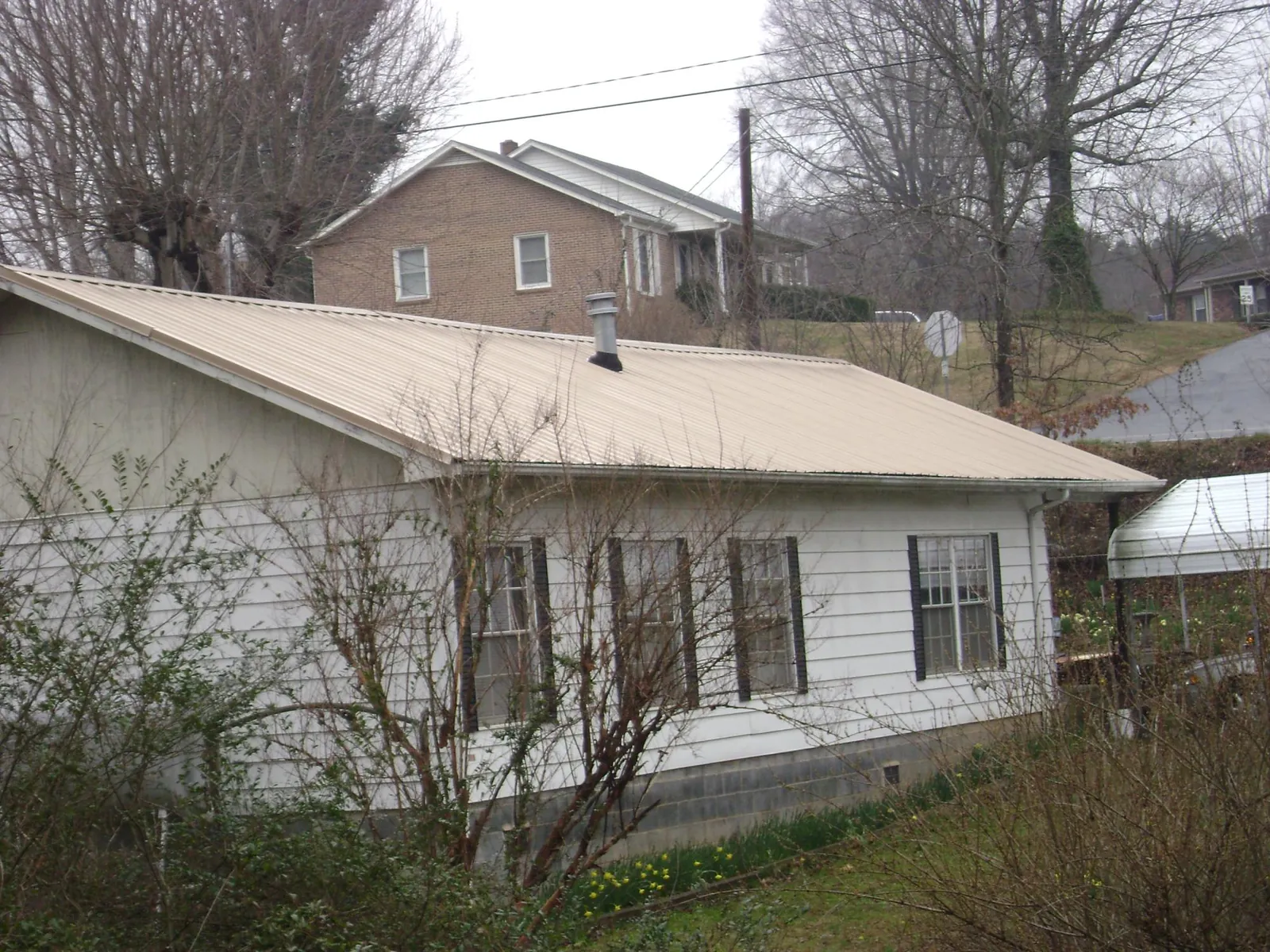 Tan metal roof on a white sided house set into a hillside — Commercial Roofing by Roofing Brothers in Rollinsville