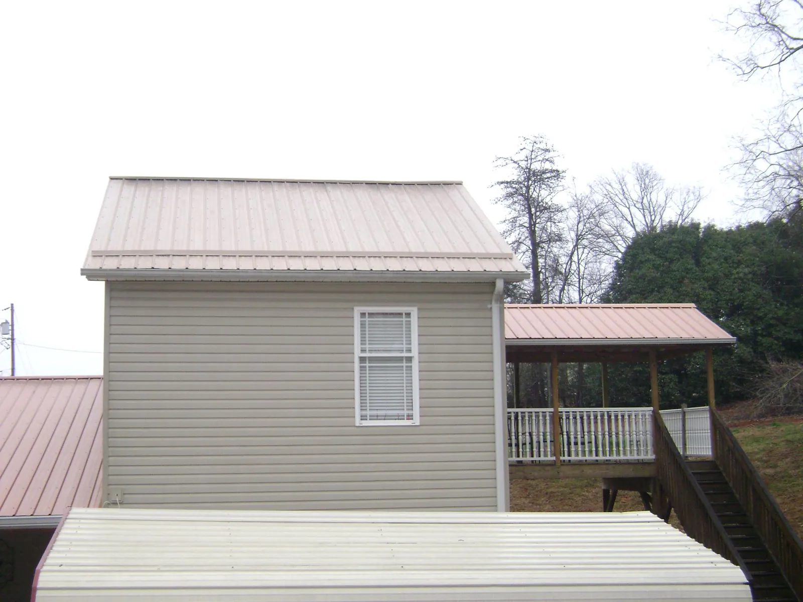 Tan metal roofs on a two story addition and attached porch, from a Roof Replacement job in Rollinsville
