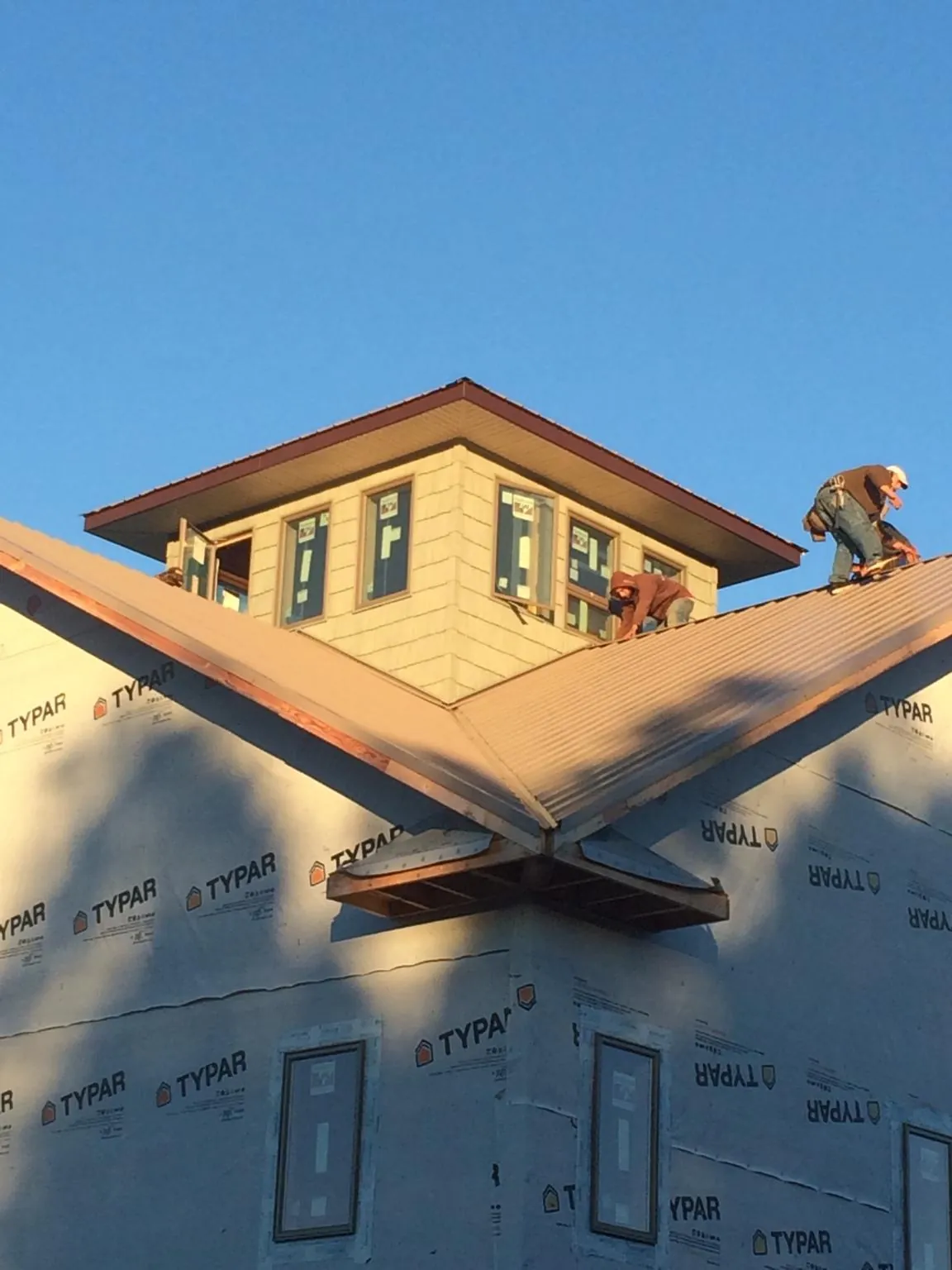 Roofers working around a rooftop cupola on a new metal roof at sunset — Roof Waterproofing in Rollinsville by Roofing Brothers